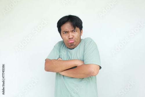 A young Asian man in a green t-shirt with an angry and annoyed expression. Isolated in gray background.
