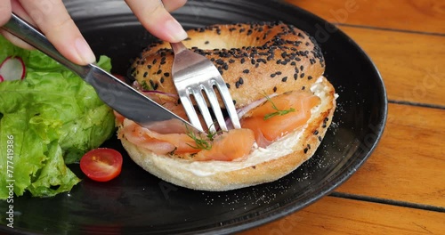 Bagel with cured salmon and cream cheese begins to be eaten with table knife and fork, close up shot. Popular meal served for breakfast of brunch, looks appetizing and fresh photo