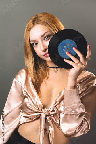 A young woman gazes through the center of a vinyl record, merging fashion with music nostalgia