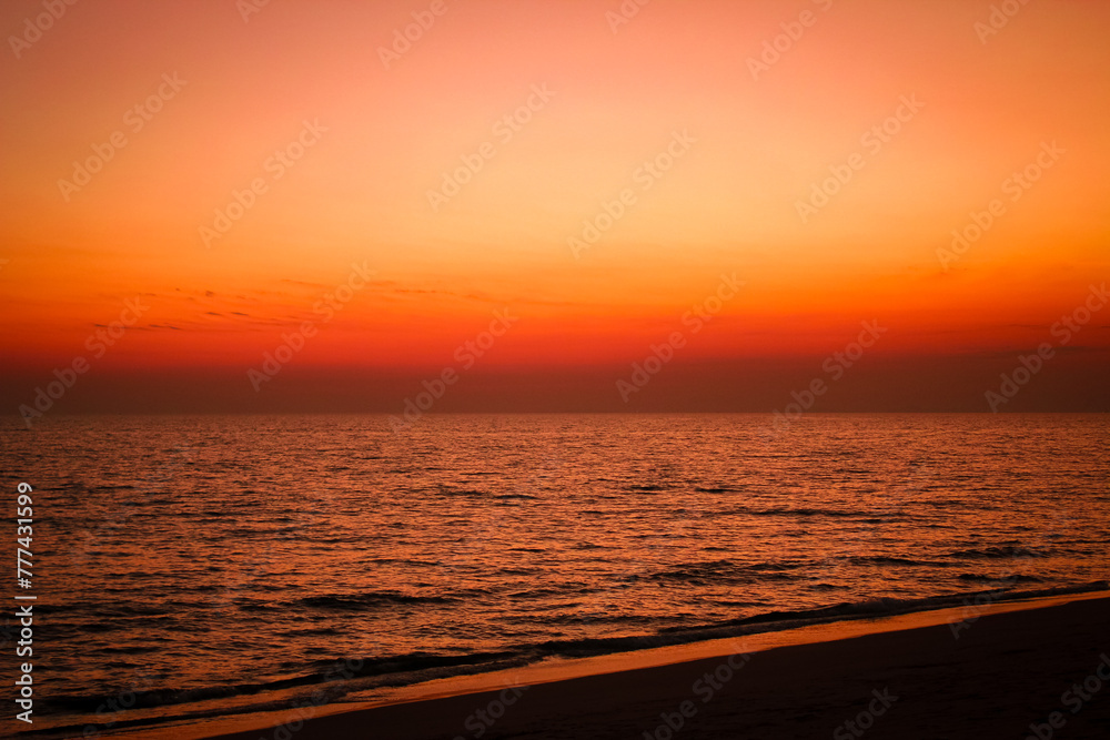 The sea after sunset has an orange glow and an orange sky with no clouds.