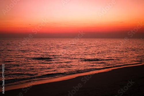 The sea after sunset has an orange glow and an orange sky with no clouds.