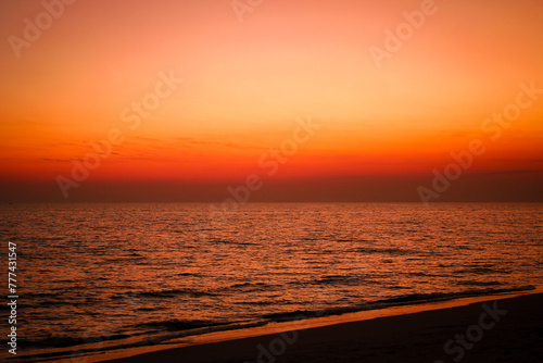 The sea after sunset has an orange glow and an orange sky with no clouds. © Birch Photography