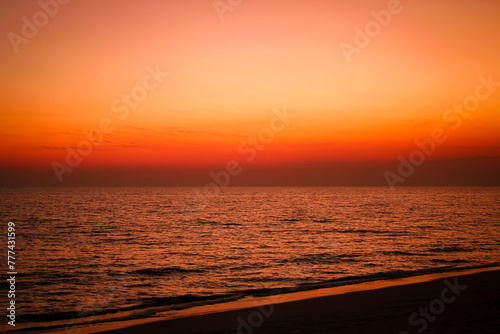 The sea after sunset has an orange glow and an orange sky with no clouds. © Birch Photography