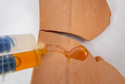 Double syringe with epoxy gel gluing and spilling on broken brown ceramic texture shards, soft focus close up