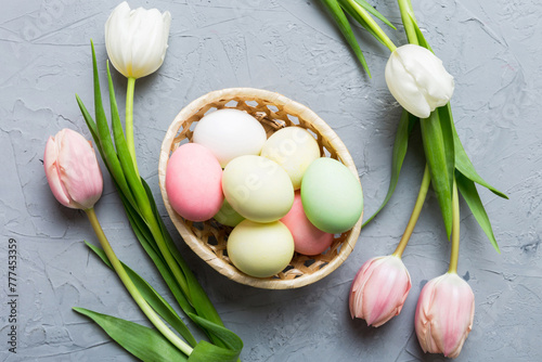 Happy Easter composition. Easter eggs in basket on colored table with yellow Tulips. Natural dyed colorful eggs background top view with copy space