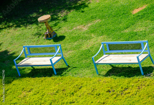 Blue benches and a side-table on grass at a park. Suitable as a background