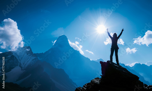 Silhouette of a woman with arms raised on top of a mountain 