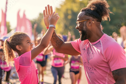 High Five for Health. In a sea of pink, a joyful father and daughter share a high five, celebrating a run, with the glow of accomplishment and familial bond on their faces photo