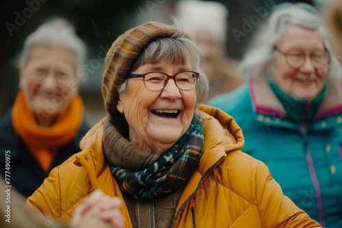 Joyful elder in yellow jacket, laughter amidst friends in park, warmth despite chill, companionship shines. Smiling senior woman with glasses, vivid attire, shares mirth with peers photo