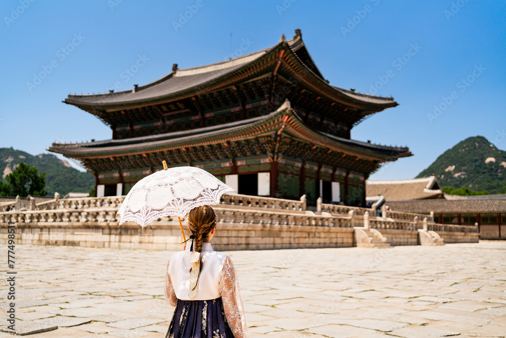 Naklejka premium Seoul, South Korea. Gyeongbokgung Palace. Woman in hanbok, traditional Korean dress, costume and clothes. Travel tour and tourism at landmark and tourist attraction. Back view of lady with umbrella.