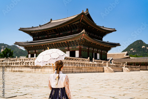 Seoul, South Korea. Gyeongbokgung Palace. Woman in hanbok, traditional Korean dress, costume and clothes. Travel tour and tourism at landmark and tourist attraction. Back view of lady with umbrella.