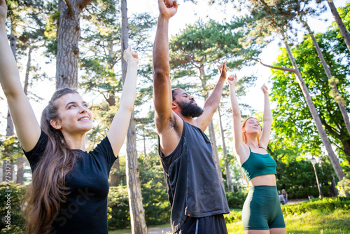 Three sporty people are in a park training and lifting arms happy © Media Lens King
