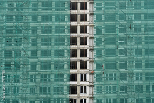 A high-rise building in the process of construction, covered with green safety netting