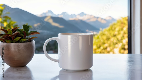 White mug sits next to small potted plant both placed on table with view of mountains in the background.