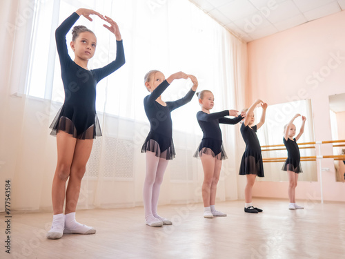 Cute little girls in black swimsuits and tutu practice ballet in class. 