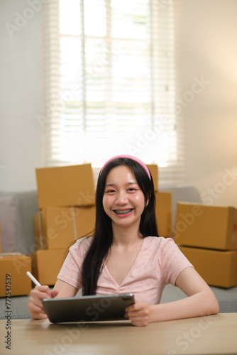 Asian business woman on sofa using a tablet checking customer order online shipping boxes at home. Starting SME Small business entrepreneur freelance. Online business, SME Work home concept.