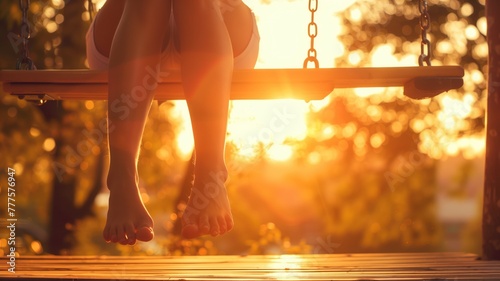 Close-up of bare feet dangling from swing at sunset, with warm lighting and sunflare