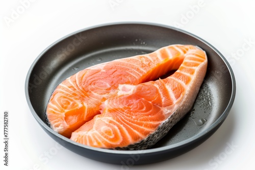 Salmon fillets seasoned with herbs and pepper, adorned with a slice of lemon, presented in a black cast iron skillet against a white background.
