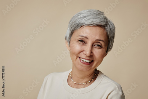 Cheerful mature woman with short grey hair and natural makeup looking at camera with smile during photo session on beige background photo