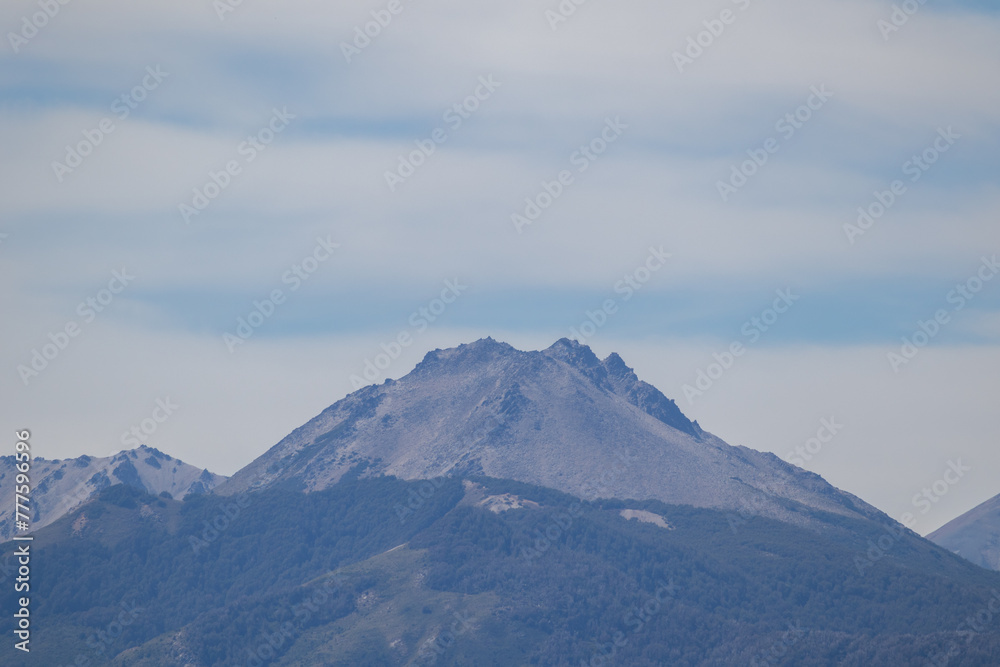 Lonely horizontal view of mountain peak with growing vegetation on the bottom, and an infinite clear blue sky on top