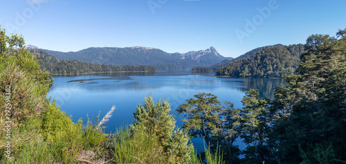 Majestic nature view of a huge clear blue lake reflecting the forest that surrounds it and the mountain range in the distance, in Lago Espejo, Argentina