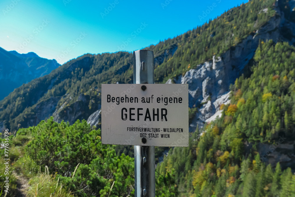 Information sign with scenic view of ountain ridges in Hochschwab massif, Styria, Austria. Board says: Attention. Danger. Enter at your own risk. Idyllic hiking trail in summer
