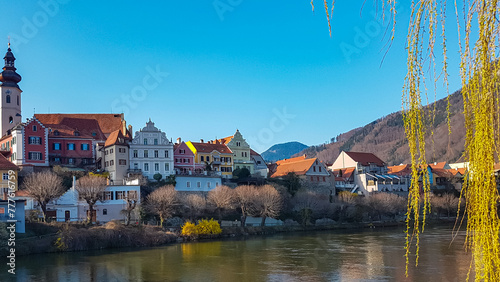 Scenic view of idyllic colourful houses next to river Mur in Frohnleiten in Styria (Steiermark), Austria. Tourism in alpine town in summer. Tree branch hanging in foreground. Travel destination