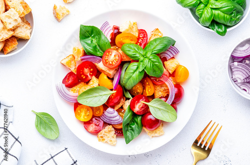 Italian salad with tomatoes, stale bread, red onion, olive oil, salt and green basil, white table background, top view