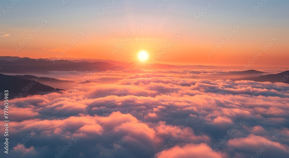   The sun sets over distant clouds in the sky fromop of a mountain peak