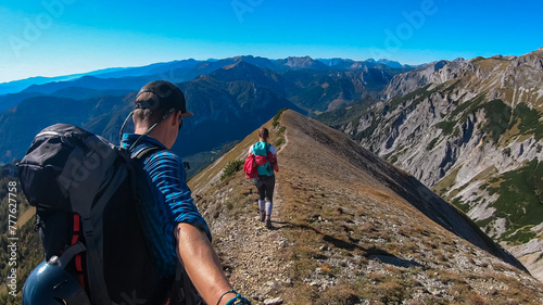 Hiker couple on idyllic hiking trail on alpine meadow with scenic view of majestic Hochschwab mountain range, Styria, Austria. Wanderlust in remote Austrian Alps. Sense of escapism, peace, reflection photo