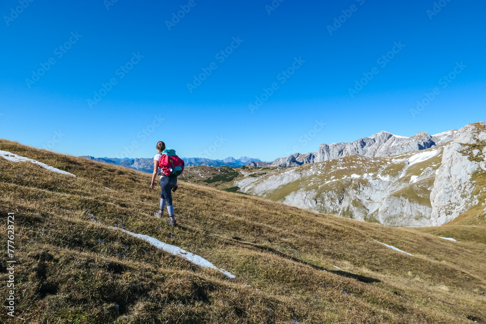 Hiker woman on scenic hiking trail along idyllic alpine meadow to Foelzkogel in wild Hochschwab massif, Styria, Austria. Wanderlust in remote Austrian Alps on sunny day. Goal achieving. Ascending hill