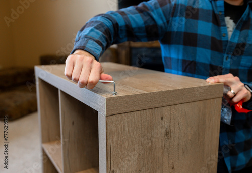 Man tightens screw while building shelves in living room of home photo