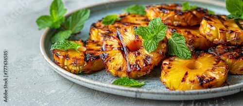 Juicy slices of grilled pineapples topped with fresh mint leaves arranged on a white plate.
