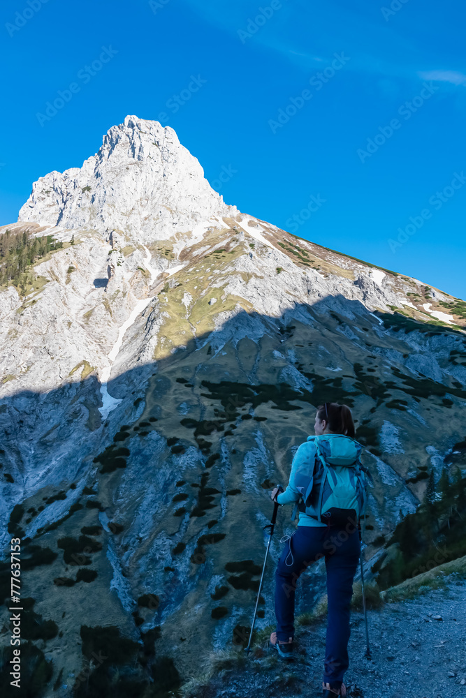 Fototapeta premium Hiker woman with panoramic view of majestic mountain peak Foelzstein in untamed Hochschwab mountain region, Styria, Austria. Scenic hiking trail on in remote Austrian Alps. Wanderlust in alpine summer