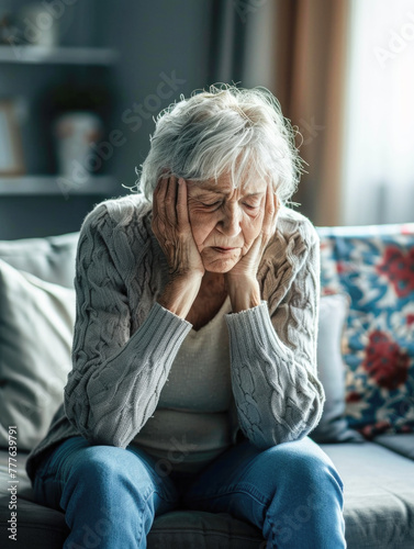 Depressed senior woman sitting alone with her head in her hands on a living room sofa at home
