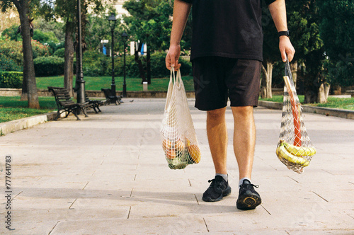 Anonymous young man walking with full mesh shopping bags after market photo