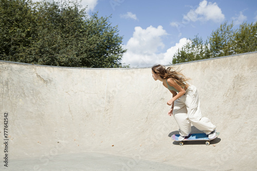 Girl riding a skateboard in a concrete bowl outdoors