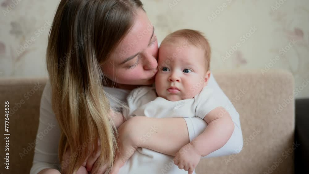 Mom holds, hugs, kisses her baby, showing her love, sitting on sofa at home. Touch of love between mother and infant. Motherhood, maternity leave, child care, childhood. Mom holds, hugs, kisses her baby, showing her love, sitting on sofa at home. Touch of love between mother and infant. Motherhood, maternity leave, child care, childhood.