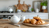 Cutting board with croissants, knife, teapot and cup on wooden table top in modern kitchen