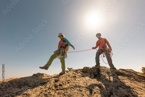 Two people are on a mountain, one of them is holding a rope. The other person is wearing a red shirt