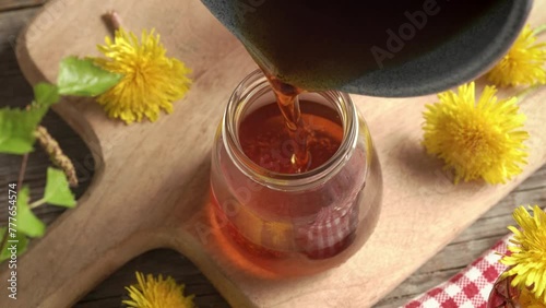 Pouring hot homemade dandelion honey - herbal syrup made from fresh Taraxacum flowers - into glass jars