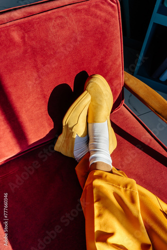 Crossed feet in yellow shoes on red armchair in daylight photo