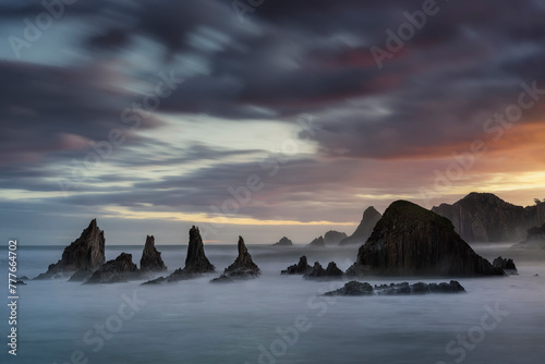 warm sunrise on the beach of Gueirua, Asturias with a dramatic sky and the high tide partially covering the rocks on the shore