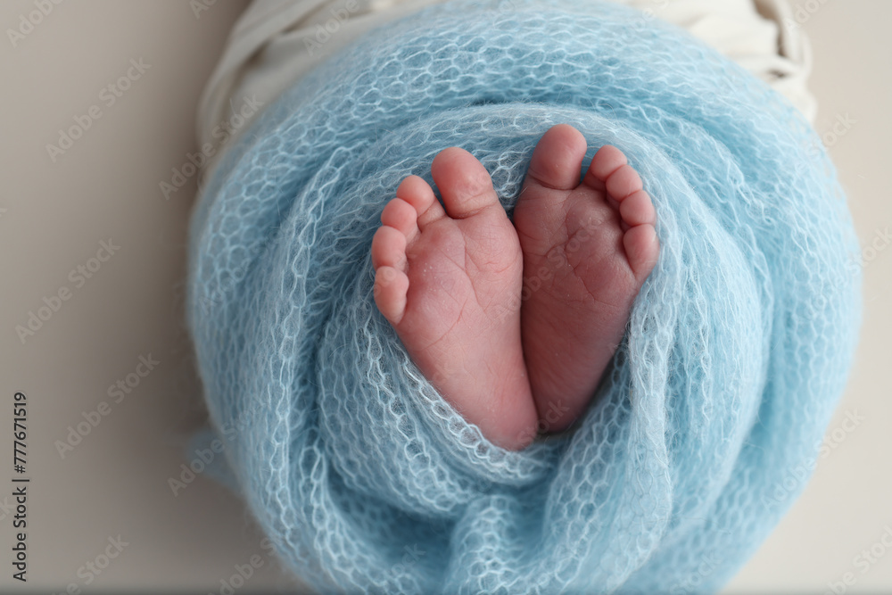The tiny foot of a newborn baby. Soft feet of a new born in a blue wool blanket. Close up of toes, heels and feet of a newborn. Macro photography. The tiny foot of a newborn baby. Soft feet of a new born in a blue wool blanket. Close up of toes, heels and feet of a newborn. Macro photography.