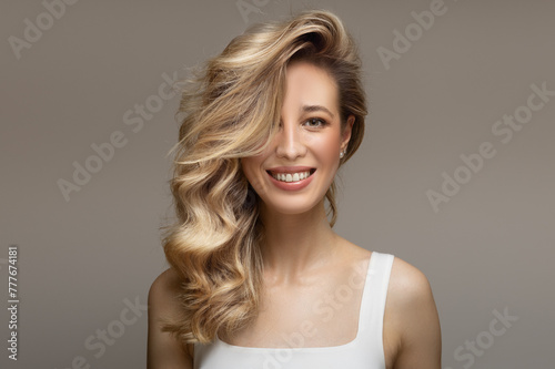 young blonde woman with curly beautiful hair smiles on a gray background