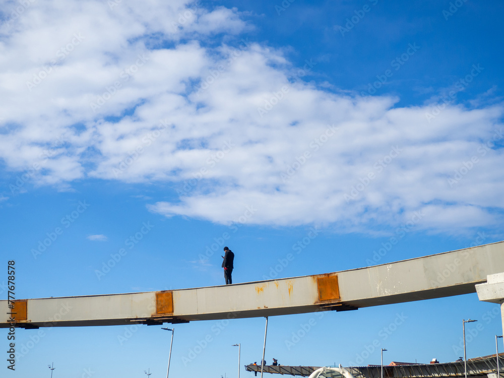 A man stands alone on an overpass under construction. At construction height. Loneliness at work. Road construction. Looking at the phone A man stands alone on an overpass under construction. At construction height. Loneliness at work. Road construction. Looking at the phone
