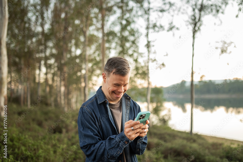 man with down syndrome using his mobile phone in a forest in nature man with down syndrome using his mobile phone in a forest in nature