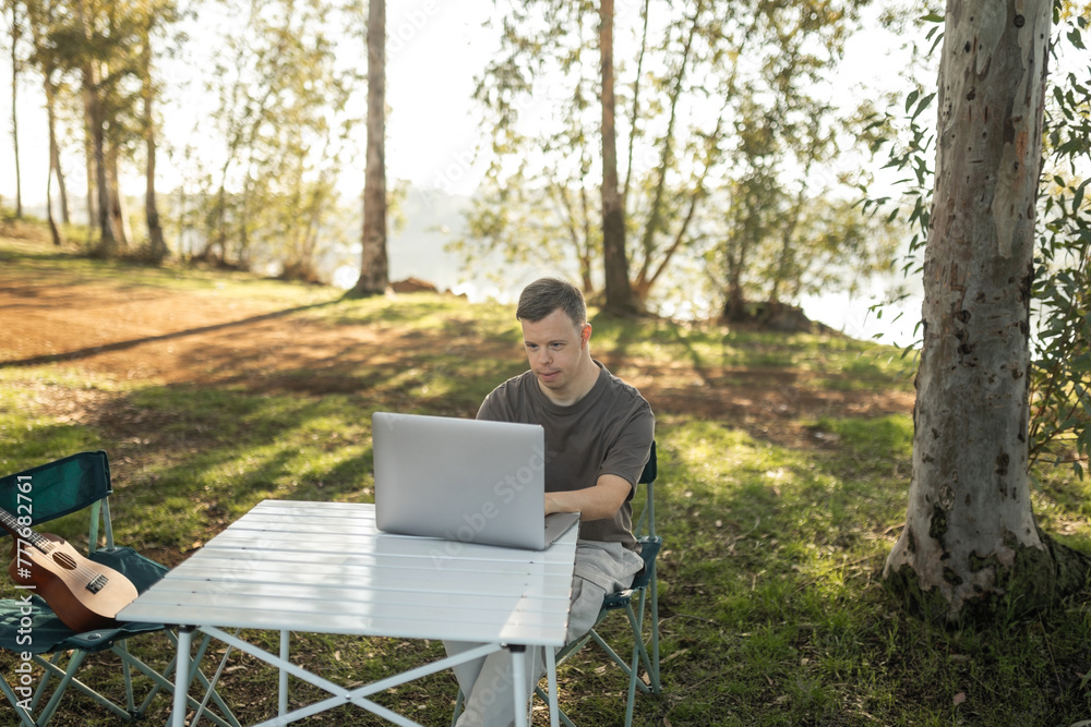 young man with down syndrome using a laptop in nature young man with down syndrome using a laptop in nature