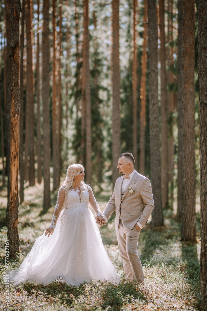 A bride and groom hold hands in a forest, with sunlight dappling through the tall trees around them... A bride and groom hold hands in a forest, with sunlight dappling through the tall trees around them...