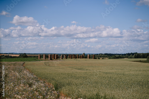 Valmiera, Latvia - Augist 13, 2023 - Rural landscape showing a wheat field with a line of old brick columns under a blue sky with scattered clouds. photo